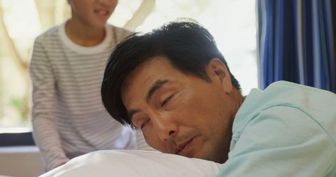 Middle-Aged Man Resting in Hospital Bed with Caregiver Nearby