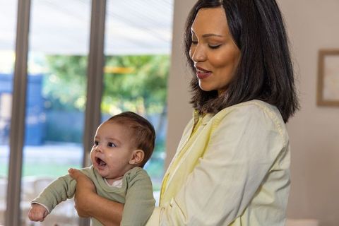 Mother holding infant daughter by sliding glass door in bright home interior