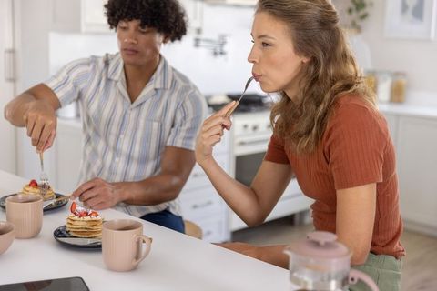 Diverse couple sharing pancakes at kitchen counter sipping coffee cozy morning together