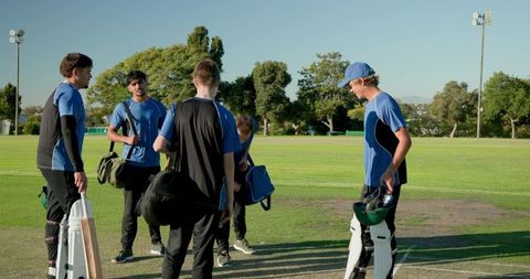 Youth cricket team gathering on pitch preparing for match in blue black uniforms outdoors