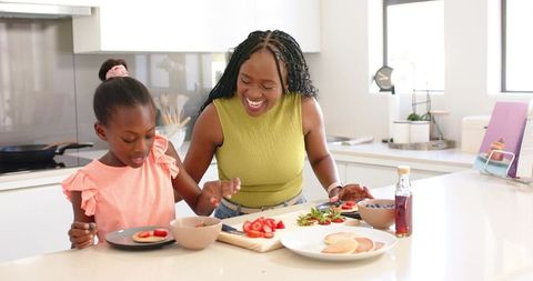 African american mom and daughter preparing pancake breakfast together in modern kitchen