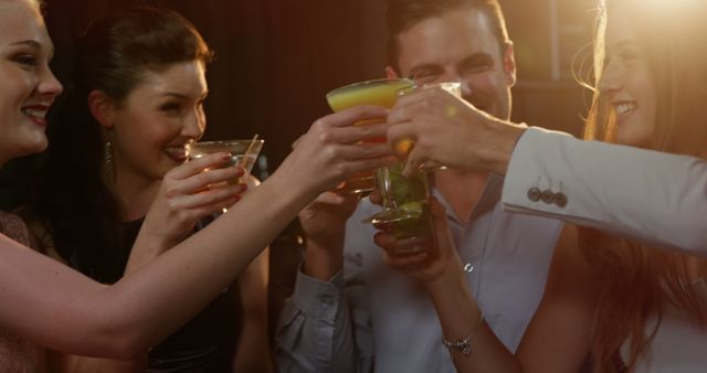 Group of friends toasting with cocktails at a nighttime celebration. Use this for social events, nightlife gatherings, joyful moments, or advertisement flyers for bars and clubs.