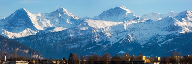 Panoramic view of a stunning snow-capped mountain range under a clear blue sky. This majestic scene is perfect for promoting tourism, outdoor activities, or any winter-related travel destinations. Ideal for use in travel websites, nature documentaries, promotional materials, and wall art.