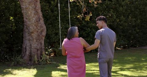 Physiotherapist assisting senior woman walking in garden