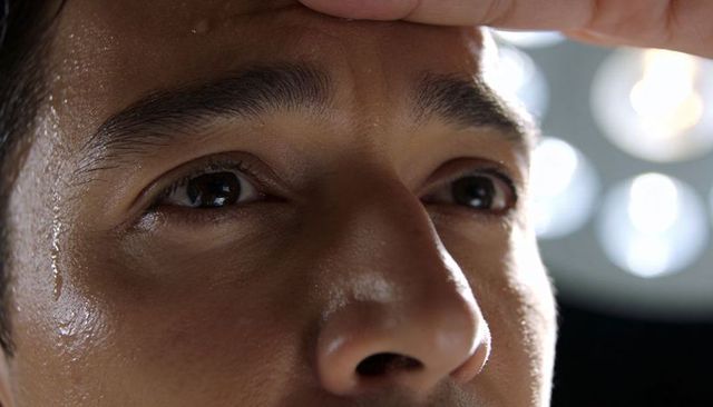 Closeup sweating adult male face with fingertip resting, lights reflecting in eyes, focus