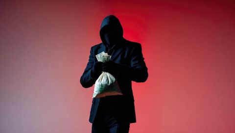 Hooded bank robber holding cash bag in mysterious red setting