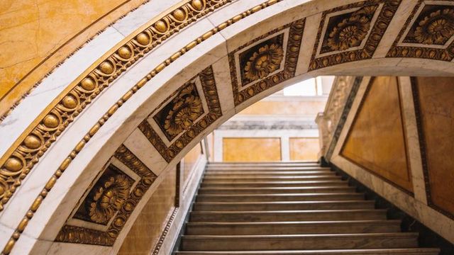 Gilded marble arch framing grand neoclassical staircase in opulent museum interior