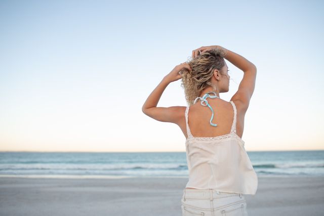 Woman standing with hands in her hair on the beach - Download Free Stock Photos Pikwizard.com