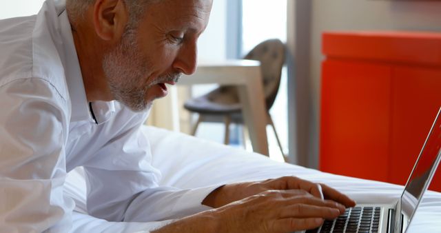 Middle Aged Man Working on Laptop While Lying on Bed in Modern Home - Download Free Stock Images Pikwizard.com