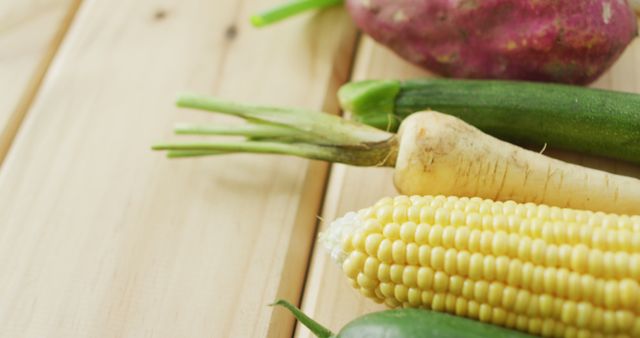 Image showing an assortment of fresh vegetables such as corn, turnip, cucumber, zucchini, and a sweet potato on a wooden surface. Ideal for use in food blogs, healthy eating promotions, farm produce advertisements, and organic produce marketing materials.