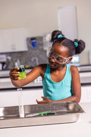 African american girl conducting colorful chemistry experiment wearing safety goggles