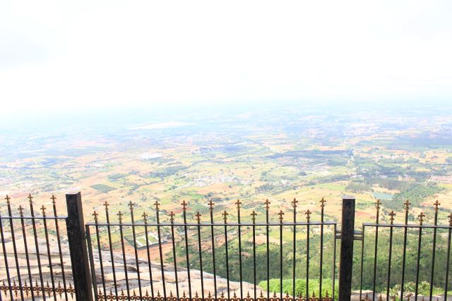 Depicts a panoramic view of the countryside seen from a mountain overlook, framed by an iron fence. Ideal for use in travel and tourism websites, brochures, nature documentaries, inspirational posters, and environmental presentations. Perfect for illustrating concepts of adventure, exploration, and scenic beauty.