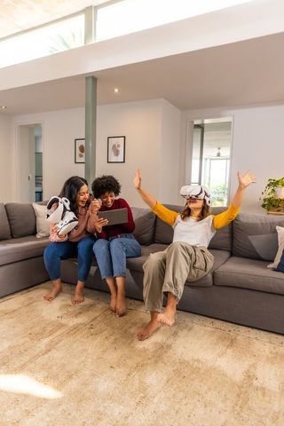 Diverse friends sharing vr headsets and tablet on cozy modern living room sofa