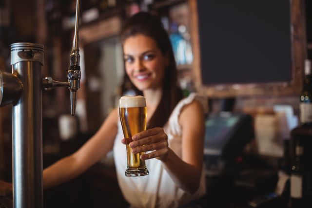 Portrait of female bar tender holding glass of beer at bar counter