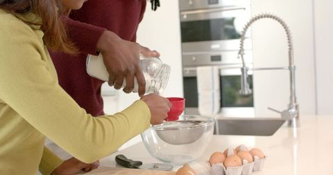 Multiracial couple pouring milk into measuring cup over bowl on kitchen island