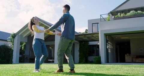 Happy couple spinning on green lawn outside modern house