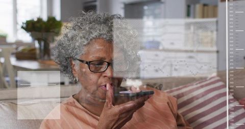 Senior woman speaking into phone on sofa wearing glasses, home and health data overlays