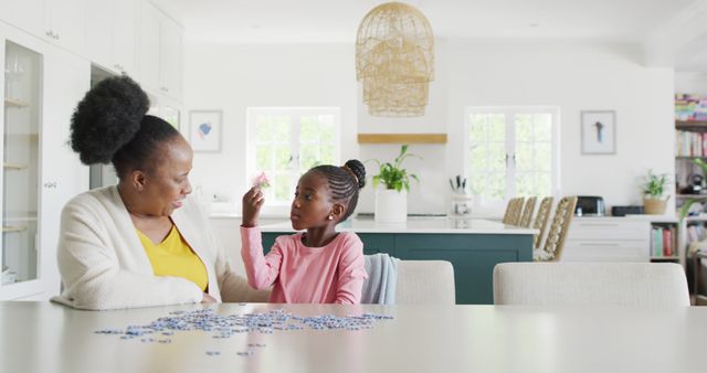 Grandmother and granddaughter are solving a puzzle together in a bright and modern kitchen. The photo captures beautiful moments of bonding and family time, showcasing love and togetherness. Ideal for use in concepts related to family values, elderly care, intergenerational activities, and home lifestyle. Perfect for websites, advertisements, and brochures focused on family, relationships, and home life.