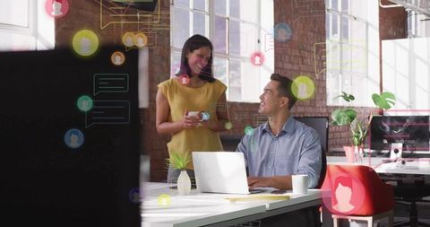 Two coworkers collaborating in loft office with laptop, coffee, digital chat overlay