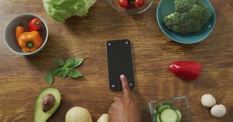 Healthy vegan ingredients surrounding smartphone on wooden table