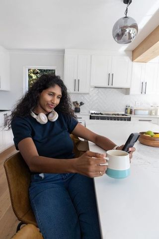 African american woman relaxing at modern kitchen island with mug and smartphone