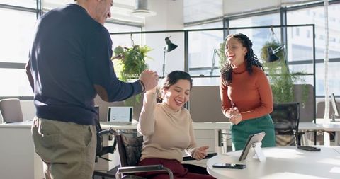 Inclusive office team celebrating success with wheelchair user and supportive team