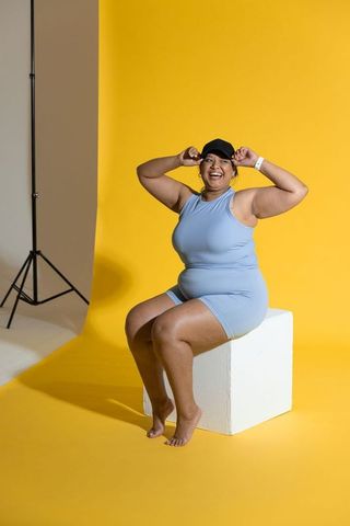Plus-size woman smiling and posing in light blue activewear on vibrant yellow backdrop