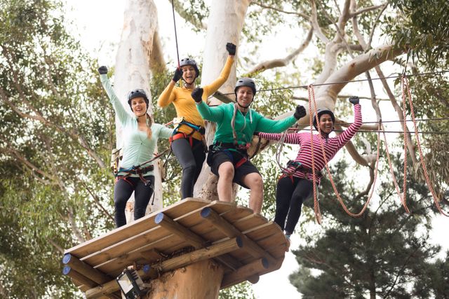 Group of friends in safety gear enjoying a thrilling zip line adventure in a lush forest park on a sunny day. Perfect for promotional materials related to outdoor activities, adventure travel, team building events, and recreational sports. Can be used to convey excitement and camaraderie in a natural setting.