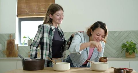 Friends cooking together in sunlit minimalist kitchen sharing joyful meal prep