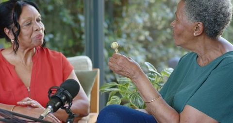 African american senior women recording relaxed home podcast conversation on sunlit sofa