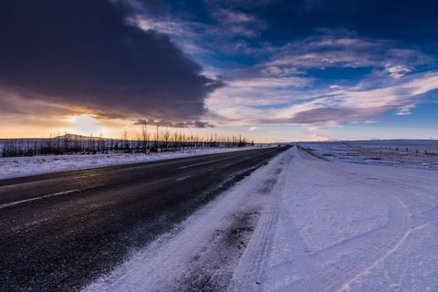 Sunset Road Cutting Through Snowy Plain Under Dramatic Winter Sky and Wide Open Horizon