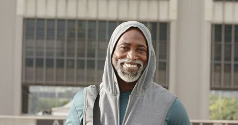 Mature african american man smiling on urban rooftop wearing hoodie and backpack strap