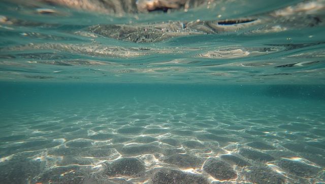Sandy seabed shimmering under turquoise water with rippled surface and light caustics