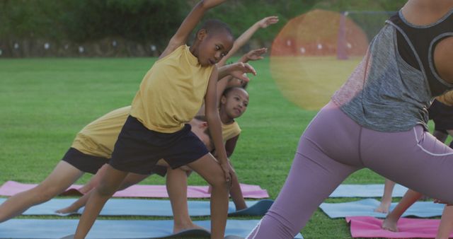 Biracial female teacher showing diverse group of schoolchildren yoga stretching exercises outdoors. children at primary school in summer.