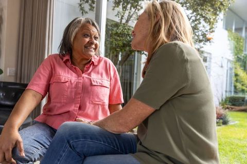 Senior female friends chatting by window enjoying relaxing conversation