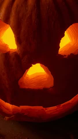 Vertical video flickering candle inside carved pumpkin casting warm glow and deep shadows Halloween