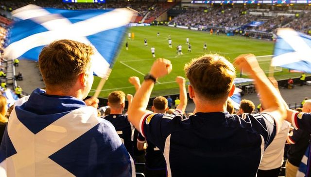Scottish football fans cheering and waving saltire flags in packed stadium stands