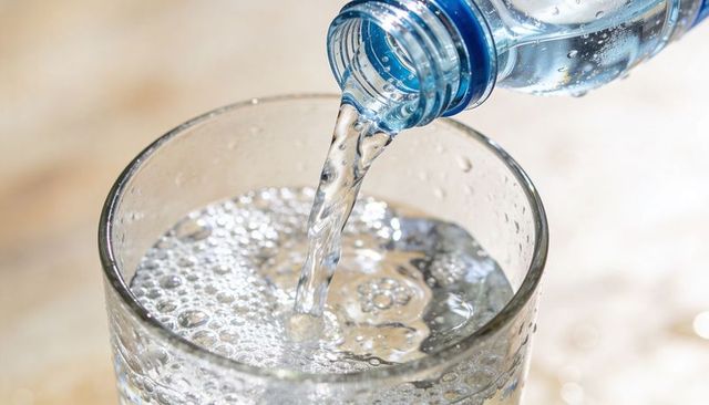 Pouring bottled water filling glass with sparkling bubbles close-up on light countertop