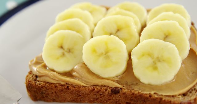 A slice of whole grain bread topped with peanut butter and banana slices sits on a plate, ready to be enjoyed. This simple and nutritious snack is a popular choice for a quick energy boost or a healthy breakfast option.