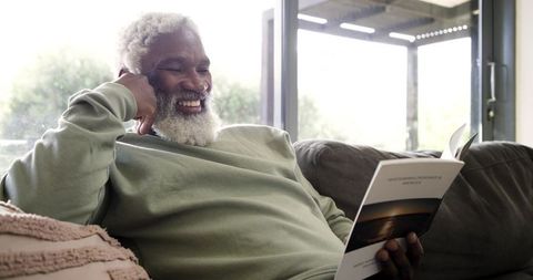 Senior man smiling while reading in modern living room