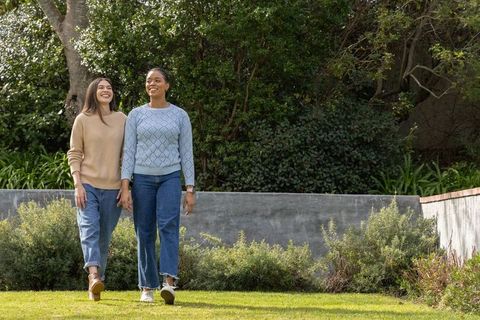 Multiracial women walking hand in hand on private backyard lawn near planter wall smiling