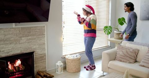 Couple Enjoying Cozy Holiday Morning by Fireplace, Woman Wearing Santa Hat