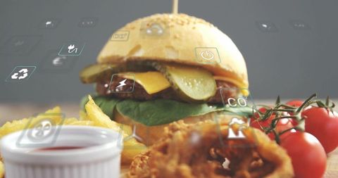 Cheeseburger sitting on sesame bun with fries, onion rings, ketchup and floating icons