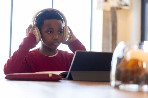 African american boy studying on tablet wearing headphones at home study table