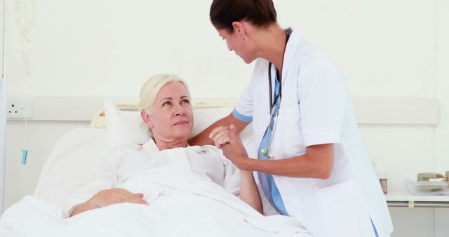 Nurse holding hands with elderly patient in hospital bed. Useful for healthcare, medical services, recovery support, nursing care, geriatric care, and hospital compassion themes.