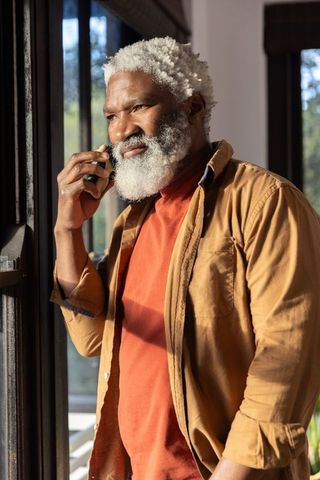 Senior african american man talking on smartphone by sunlit window, thoughtful casual moment