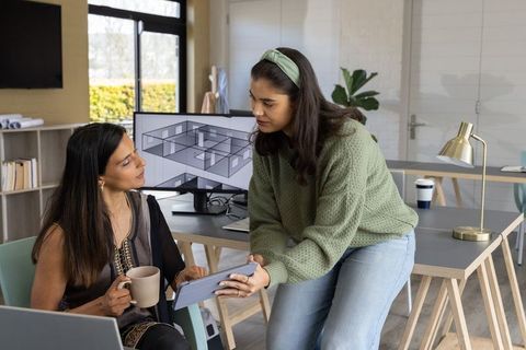Diverse coworkers collaborating over tablet reviewing architectural floorplan in studio