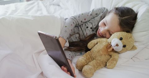 Young Girl Using Tablet in Bed with Teddy Bear