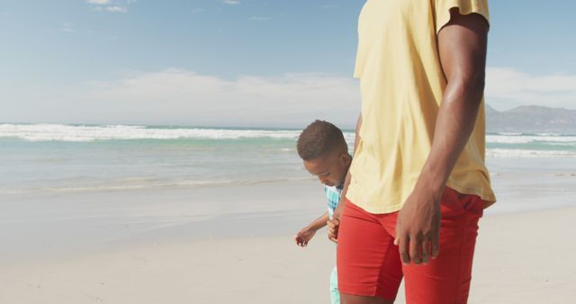 African american son holding his father's hand while walking on the beach. family travel and vacation concept