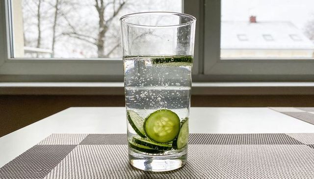 Sparkling cucumber water in tall glass on window table with snowy roof background